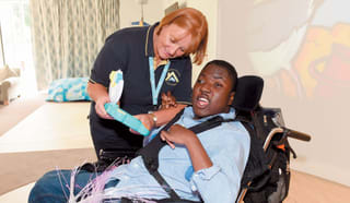 Boy in wheelchair laughing with Alexander Devine nurse.